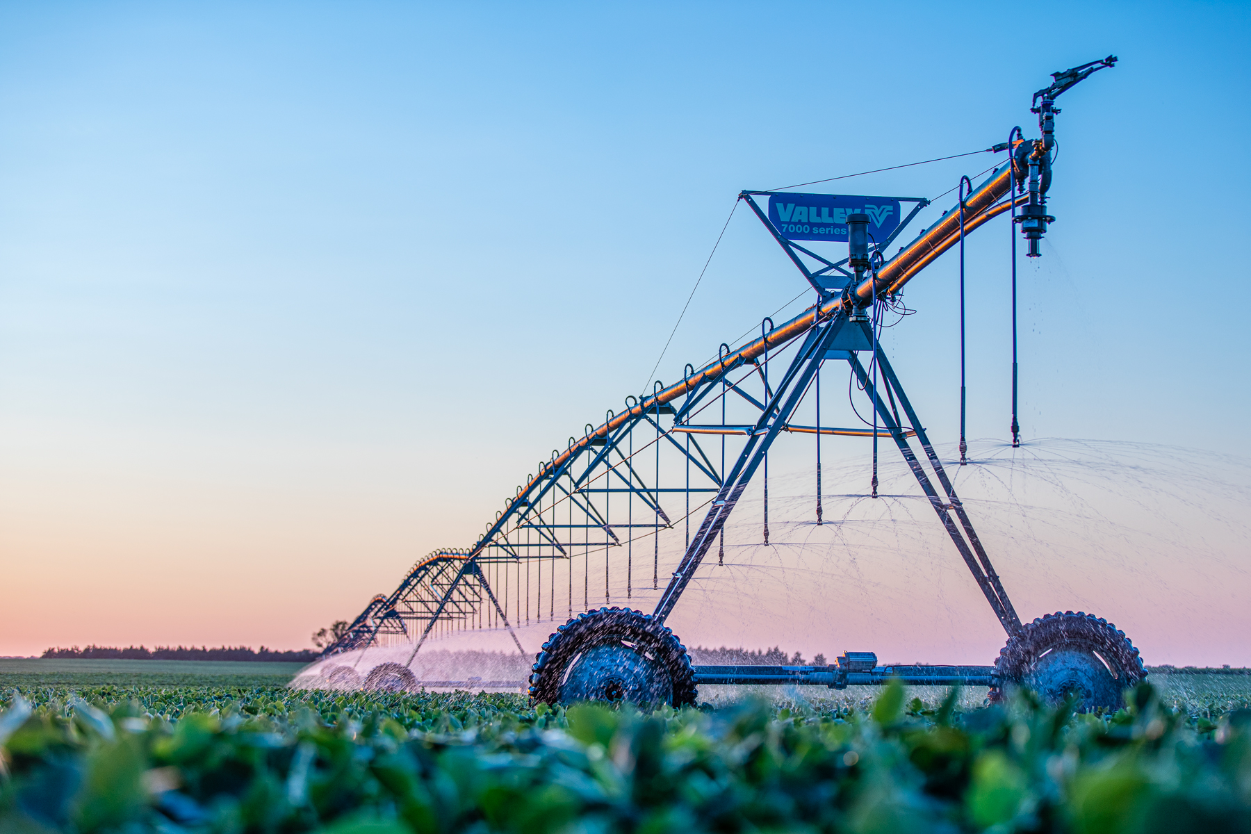 Center-pivot irrigation system watering a green field at sunset